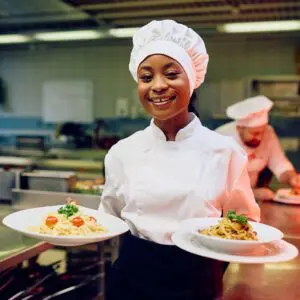 Chef holding plates of pasta dishes, smiling.