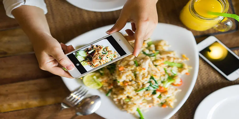 Person photographing a plate of fried rice with vegetables using a smartphone.