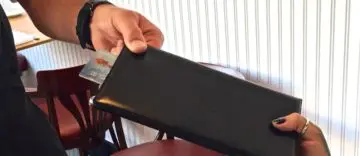 Person holding a black wallet or clutch.