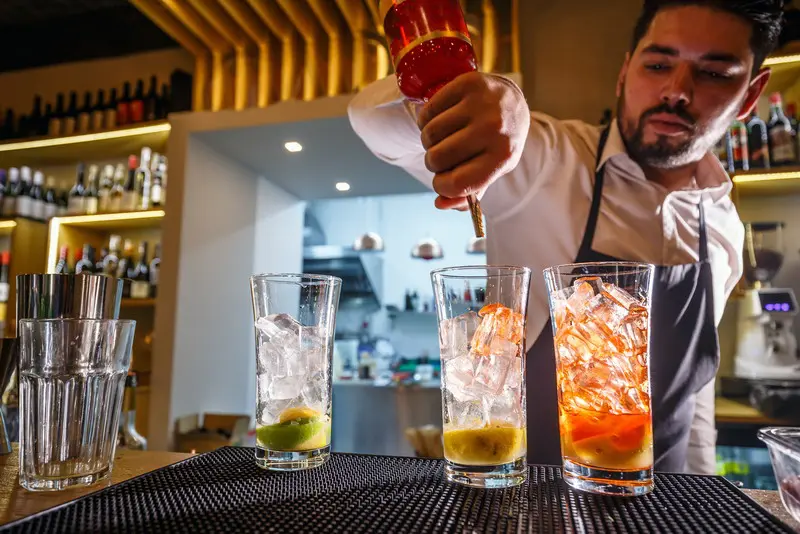 Bartender pouring drinks into glasses with ice.