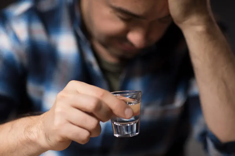 Man holding a shot glass, looking down.