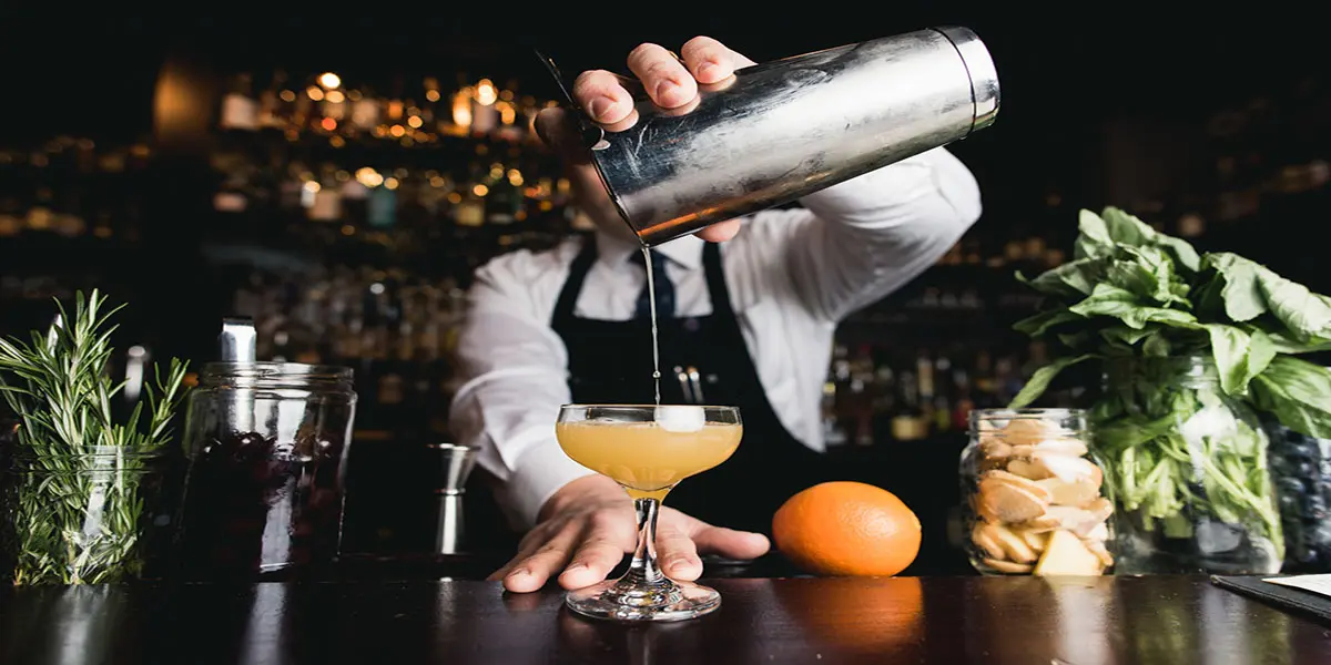 Bartender pouring cocktail at a bar counter.
