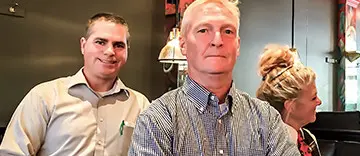 Two men posing indoors, one in the foreground and one in the background.