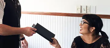 Hand passing a black rectangular box to another person indoors.