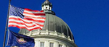 American flag waving near a historic domed building under a clear blue sky.