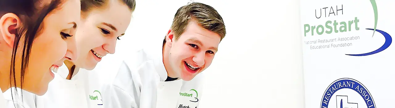 Three students smiling in chef uniforms.