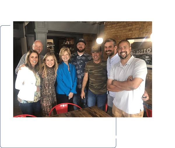 Group of seven people smiling indoors at a casual gathering.