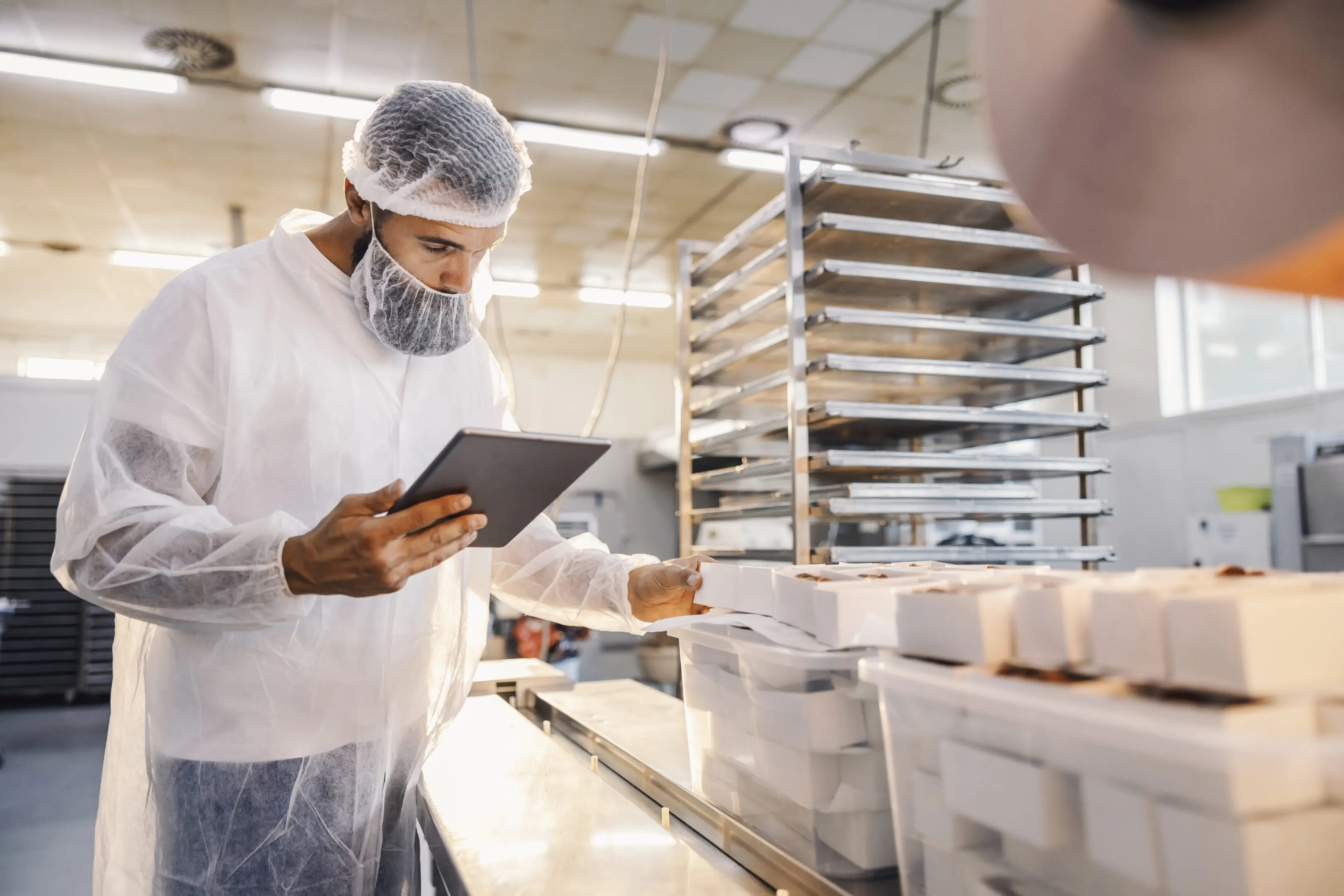 Worker in protective gear inspecting food production with a tablet.