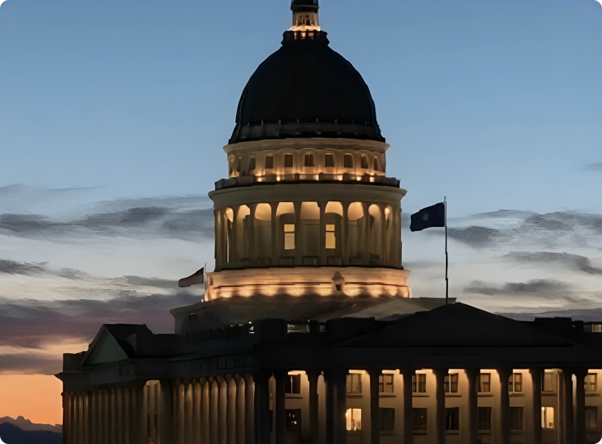 Illuminated capitol building dome at dusk with flags waving.