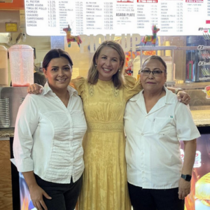 Three women posing happily at a colorful indoor market or store.